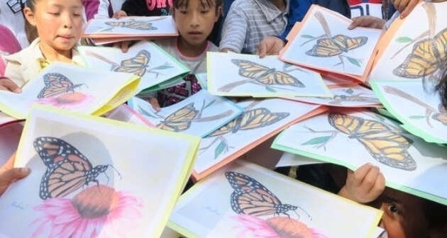 Girls with papers depicting monarchs and trees work on their activities