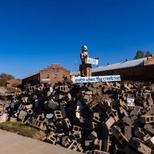 A statue standing among rubble with signed that say Hope...even when the creek rises