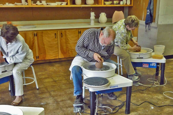 Three adults shaping pottery on pottery wheels